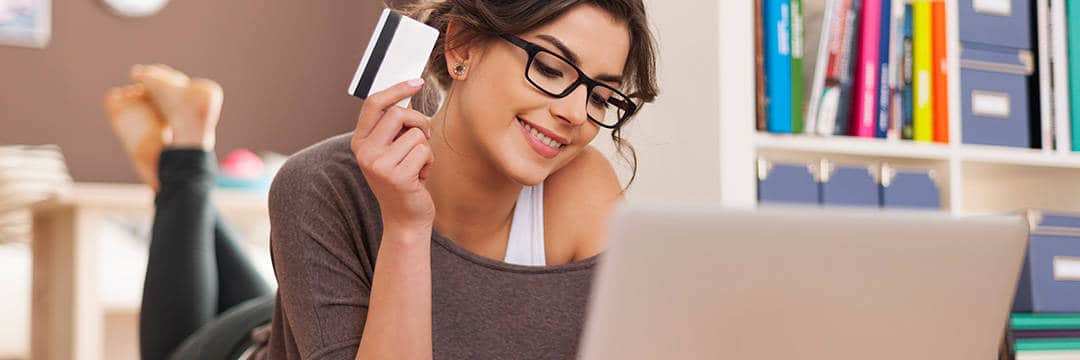 Chica joven, con la tarjeta de crédito en la mano, comprando gafas online desde su portátil