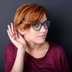 Chica con gafas graduadas con la mano en la oreja para escuchar noticias y novedades